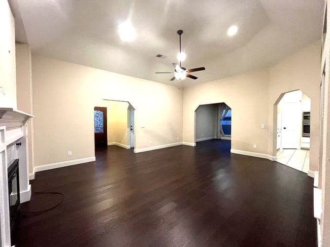Unfurnished living room featuring a ceiling fan, arched walkways, a glass covered fireplace, and wood finished floors | Image 26