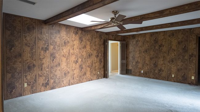 Carpeted empty room featuring wooden walls, beam ceiling, a skylight, and a ceiling fan | Image 23