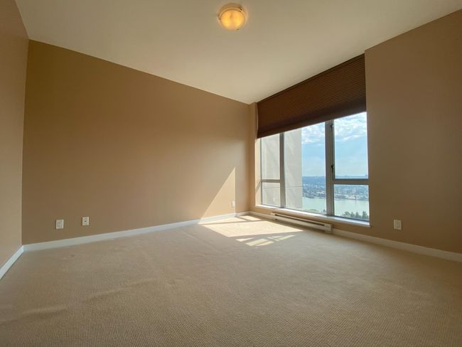 Empty room with a baseboard heating unit, carpet floors, baseboards, a water view, and lofted ceiling | Image 7