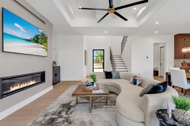 Living area featuring a tray ceiling, a glass covered fireplace, light wood-style flooring, recessed lighting, and stairway | Image 4