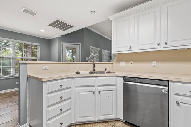 Kitchen with stainless steel dishwasher, a peninsula, crown molding, white cabinetry, and light countertops | Image 8