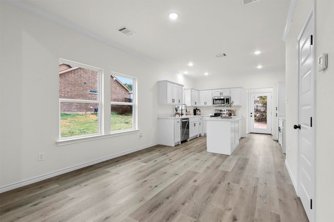 Kitchen with stainless steel appliances, light hardwood / wood-style flooring, a kitchen island, white cabinets, and crown molding | Image 12