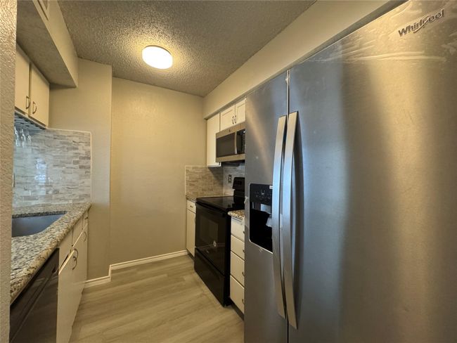 Kitchen with black appliances, light wood finished floors, tasteful backsplash, a textured ceiling, and white cabinetry | Image 6