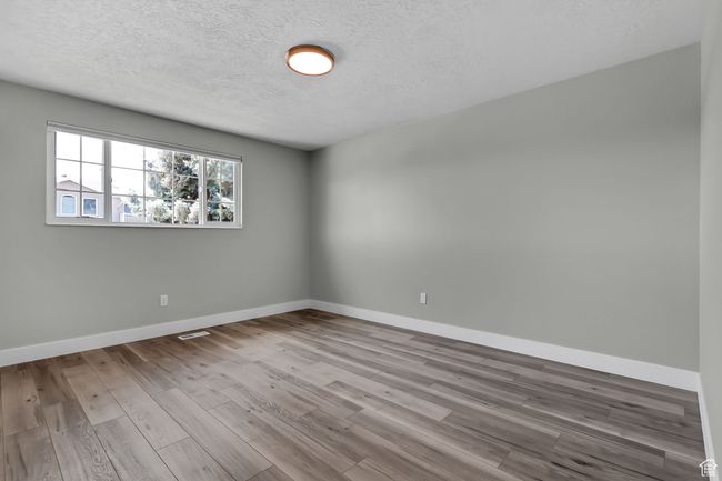 Empty room with baseboards, visible vents, wood finished floors, and a textured ceiling | Image 15