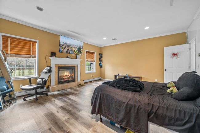 Bedroom featuring crown molding, recessed lighting, wood finished floors, a baseboard heating unit, and a tile fireplace | Image 20