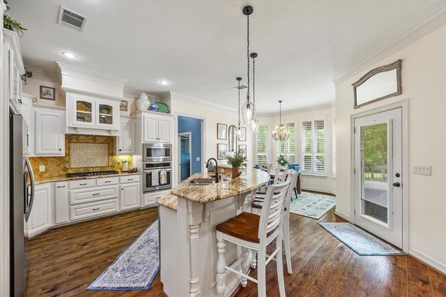 Kitchen with appliances with stainless steel finishes, white cabinets, backsplash, dark hardwood / wood-style flooring, and a kitchen island with sink | Image 18