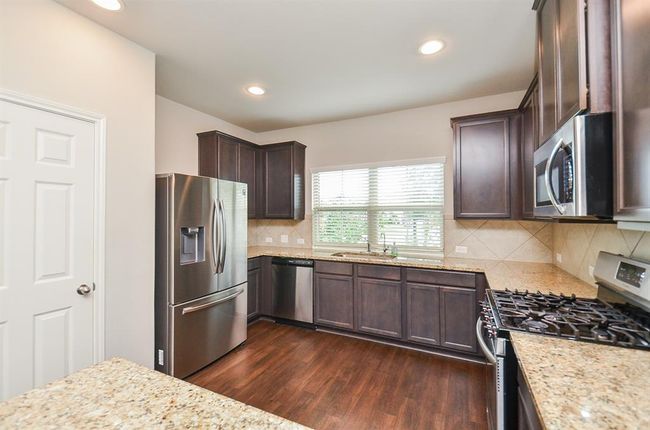 The compact, yet truly workable kitchen features rich dark cabinetry, up and down, with creamy granite counter tops and good looking tile backsplash. | Image 7