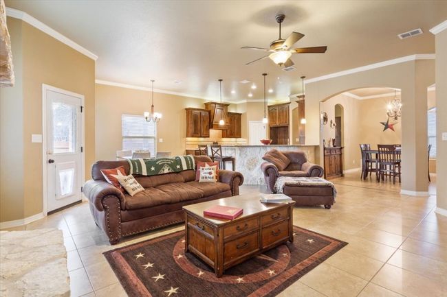 Living room featuring visible vents, ceiling fan with notable chandelier, arched walkways, light tile patterned flooring, and baseboards | Image 13