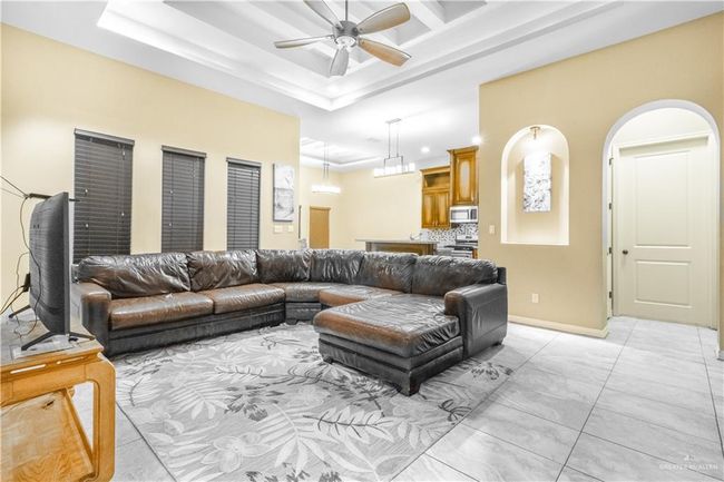 Living room with a raised ceiling, light tile patterned floors, and ceiling fan | Image 10