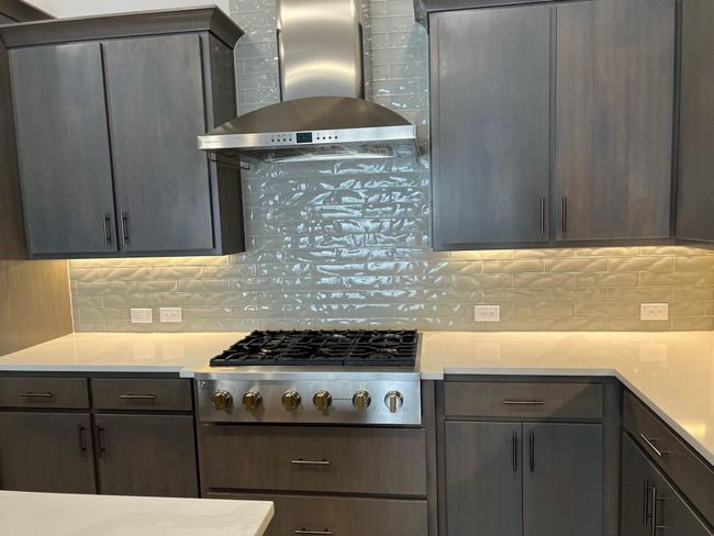 Kitchen featuring wall chimney exhaust hood, stainless steel gas stovetop, decorative backsplash, and light countertops | Image 10