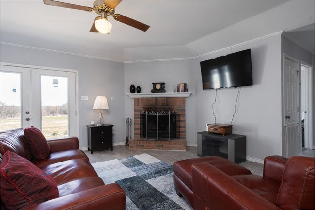 Living room with french doors, a fireplace, ceiling fan, baseboards, and ornamental molding | Image 5