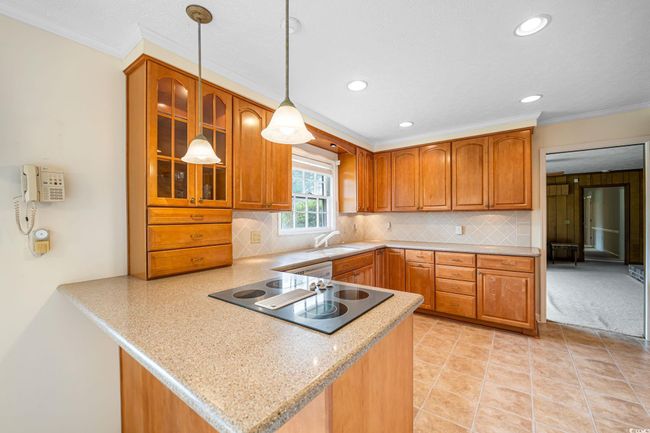 Kitchen with black electric cooktop, a sink, brown cabinetry, glass insert cabinets, and a peninsula | Image 7