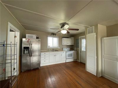 Kitchen with sink, white cabinets, dark wood-type flooring, white appliances, and ceiling fan | Image 3