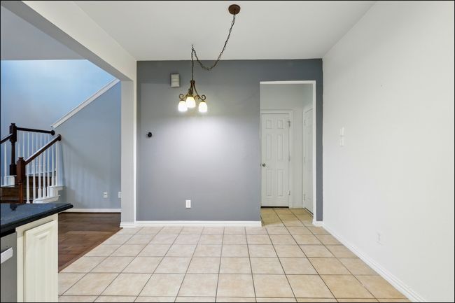 Unfurnished dining area featuring baseboards, light tile patterned floors, a notable chandelier, and stairway | Image 12