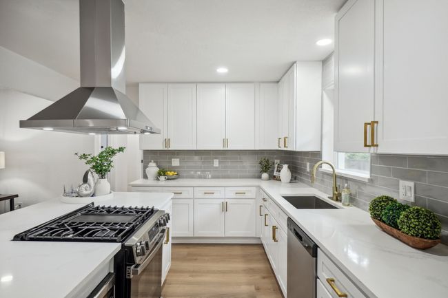 Kitchen with island range hood, a sink, stainless steel appliances, white cabinetry, and backsplash | Image 16