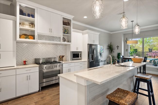 Kitchen with tasteful backsplash, crown molding, pendant lights over breakfast bar, stainless steel appliances, and gas range | Image 8