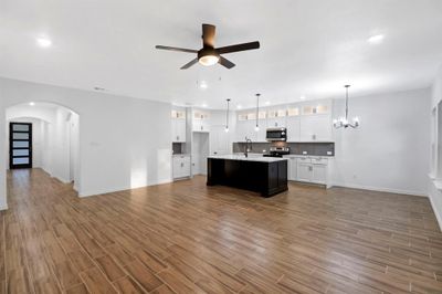 Kitchen featuring electric stove, white cabinets, ceiling fan with notable chandelier, an island with sink, and pendant lighting | Image 3