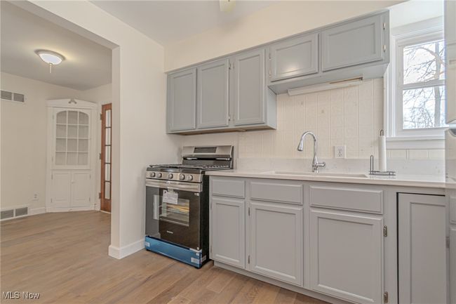Kitchen featuring gray cabinetry, sink, stainless steel gas range, decorative backsplash, and light wood-type flooring | Image 6