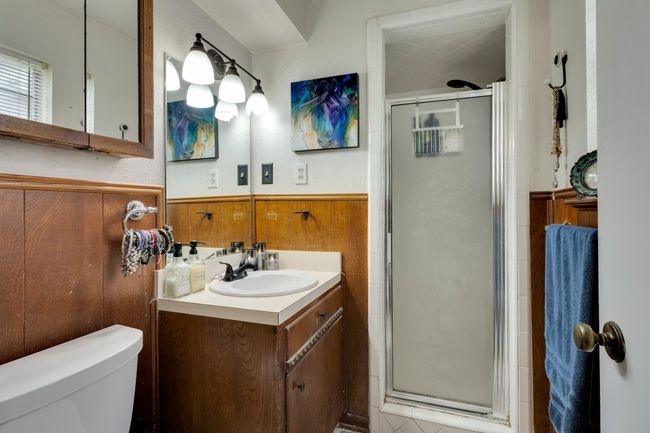 Full bath with a shower stall, wainscoting, vanity, toilet, and wood walls | Image 15