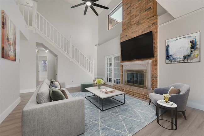 Living room with a ceiling fan, wood finished floors, stairs, a brick fireplace, and a high ceiling | Image 5