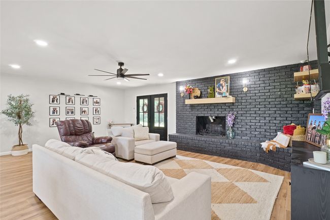 Living area with wood finished floors, recessed lighting, a ceiling fan, a fireplace, and brick wall | Image 9