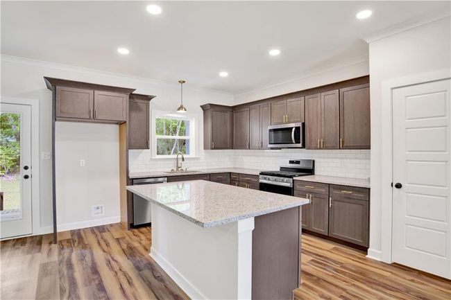 Kitchen featuring dark brown cabinetry, appliances with stainless steel finishes, a sink, a center island, and tasteful backsplash | Image 13