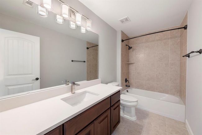 This upstairs full bath features warm tile surround, a soaking tub/shower combo, sleek quartz counters, and modern fixtures—ideal for guests or family comfort. | Image 34