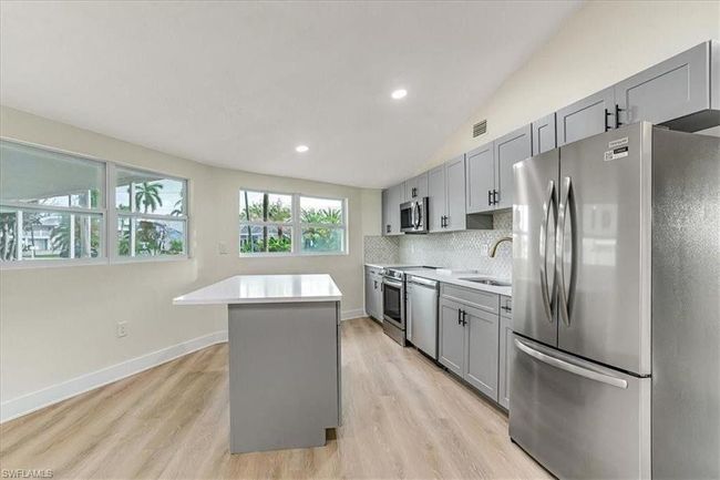 Kitchen with stainless steel appliances, gray cabinets, a kitchen island, light countertops, and lofted ceiling - Virtually Edited | Image 16