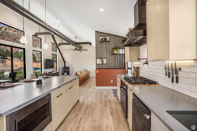 Kitchen featuring wall chimney exhaust hood, modern cabinets, light wood finished floors, black appliances, and backsplash | Image 15