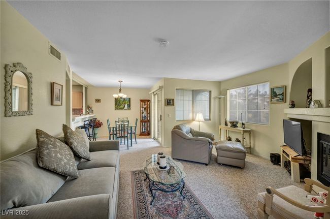 Carpeted living room featuring a chandelier, a glass covered fireplace, and visible vents | Image 22