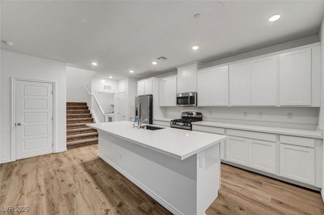 Kitchen with stainless steel appliances, light wood-style floors, a sink, white cabinetry, and a center island with sink | Image 15