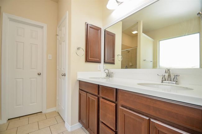 This primary bathroom features a double vanity with elegant dark wood cabinets, a large mirror, and modern fixtures. It has a neutral color palette and tiled floor, offering a spacious and bright atmosphere. | Image 19