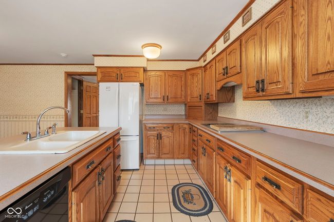 kitchen with wallpapered walls, black dishwasher, freestanding refrigerator, a sink, and brown cabinets | Image 13