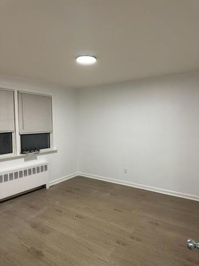 Empty room featuring radiator heating unit, baseboards, and dark wood-style flooring | Image 4