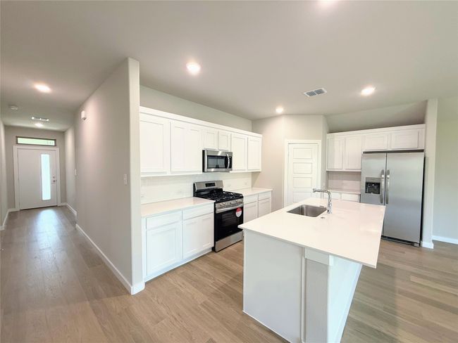 Kitchen featuring appliances with stainless steel finishes, light wood-style floors, white cabinets, an island with sink, and light countertops | Image 6