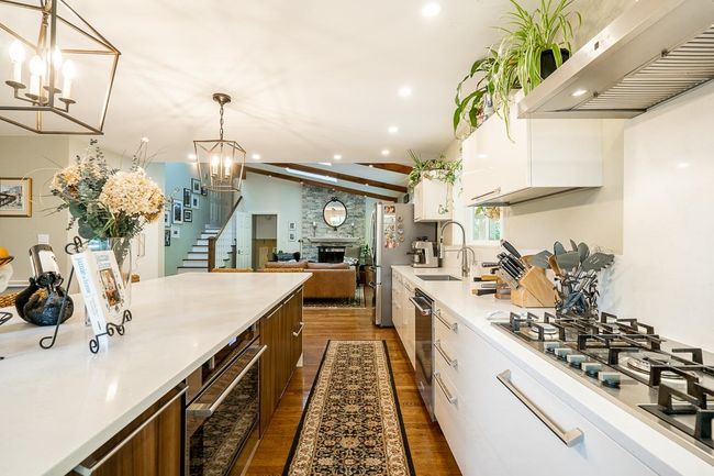 Kitchen with under cabinet range hood, dark wood-style floors, white cabinetry, light countertops, and stainless steel appliances | Image 8