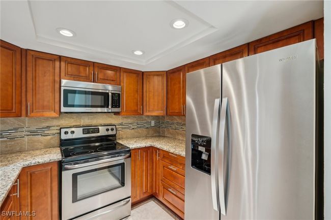 Kitchen with appliances with stainless steel finishes, recessed lighting, light stone counters, brown cabinetry, and decorative backsplash | Image 14