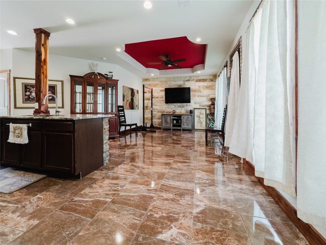 Kitchen with a ceiling fan, light stone counters, a tray ceiling, recessed lighting, and a stone fireplace | Image 13