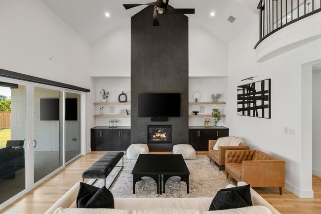 Living area with high vaulted ceiling, a ceiling fan, light wood finished floors, a fireplace, and built in features | Image 8