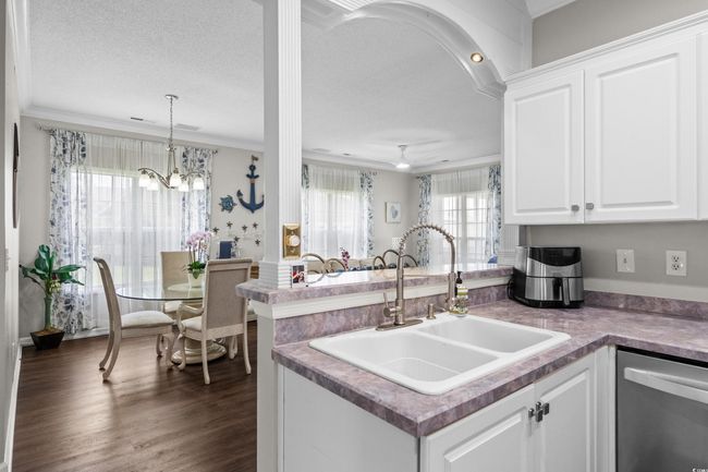 Kitchen featuring a sink, stainless steel dishwasher, crown molding, a peninsula, and white cabinetry | Image 15
