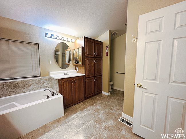 Full bath with a textured ceiling, visible vents, toilet, vanity, and a garden tub | Image 11