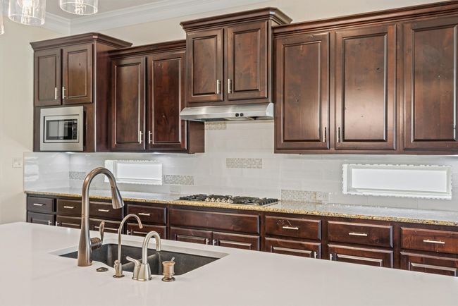 Spacious, open kitchen features decorative backsplash, dark brown cabinetry, crown molding, stainless steel appliances, and contemporary light fixture | Image 17