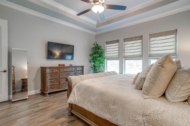 Bedroom featuring light wood-type flooring, ornamental molding, ceiling fan, and a raised ceiling | Image 31