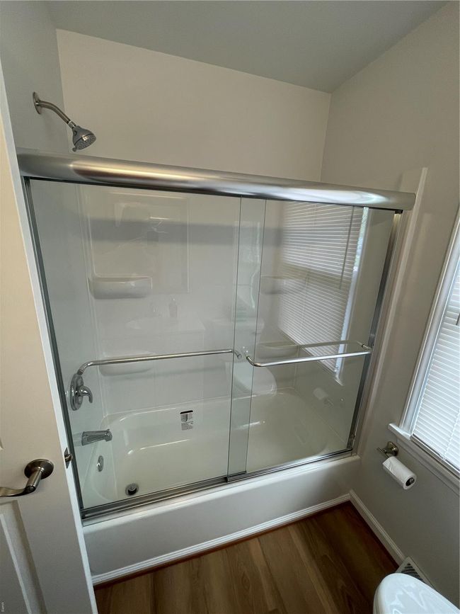 Bathroom featuring shower / bath combination with glass door, wood finished floors, toilet, and baseboards | Image 24