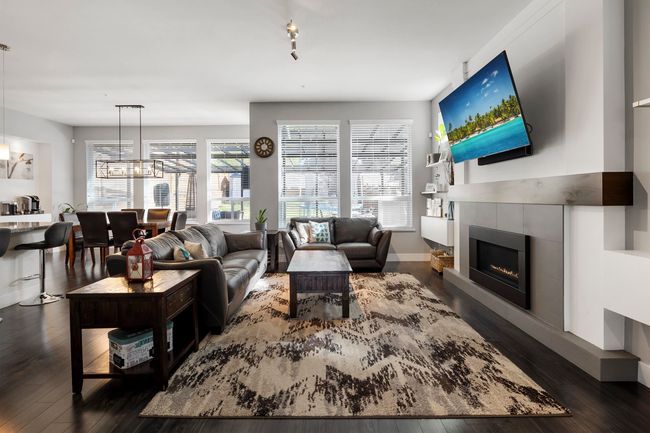 Living room with dark wood-type flooring, a notable chandelier, a fireplace, and baseboards | Image 5