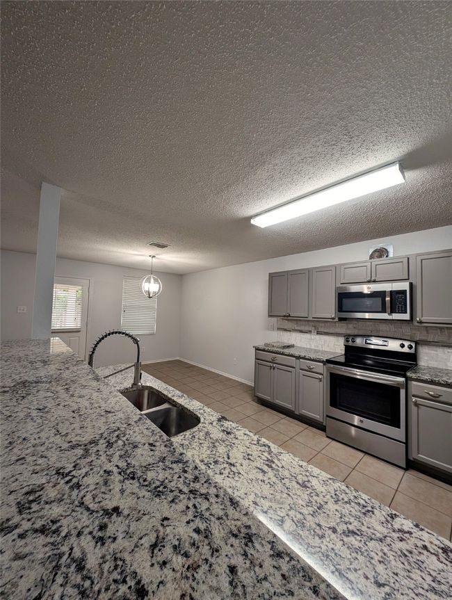 Kitchen featuring appliances with stainless steel finishes, gray cabinets, light tile patterned floors, a sink, and a textured ceiling | Image 7
