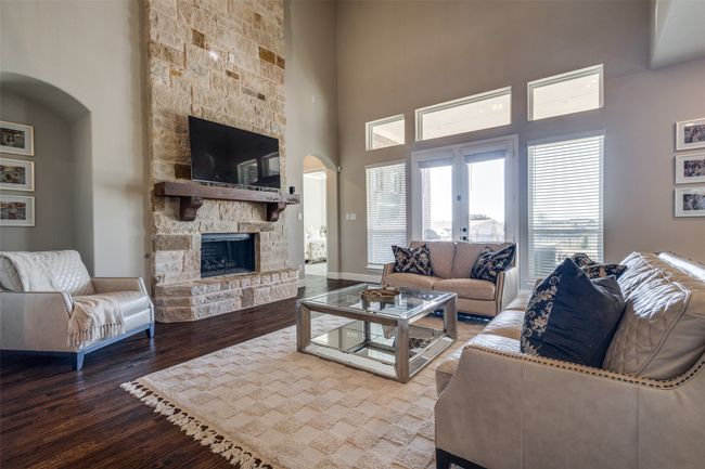 Living room with hardwood / wood-style flooring, a stone fireplace, a towering ceiling, and french doors | Image 10