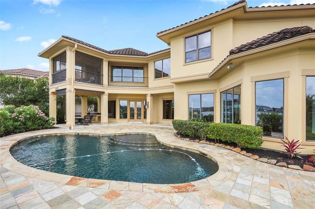 This photo showcases the luxurious two-story home with a spacious backyard featuring a salt water pool surrounded by a stone patio. Large windows and a covered outdoor seating area enhance the elegant design, offering a perfect blend of comfort and style for outdoor living. | Image 45