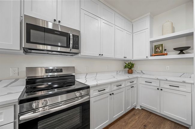 Kitchen with light stone counters, open shelves, white cabinets, appliances with stainless steel finishes, and dark wood-style flooring | Image 14