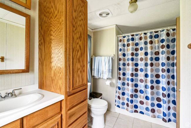 Full bath featuring vanity, toilet, tile patterned flooring, a shower with shower curtain, and wallpapered walls | Image 16